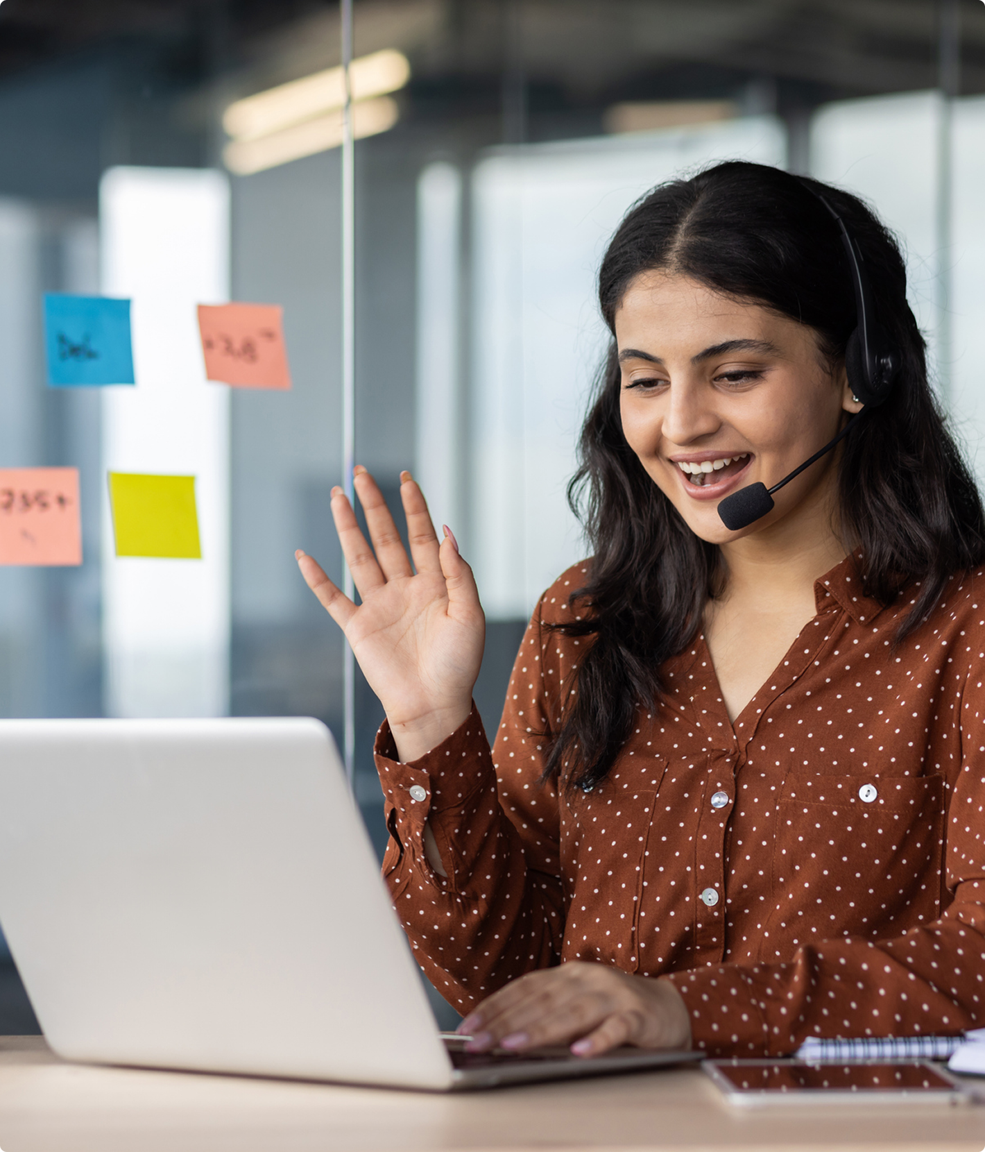 Woman with headset waving at laptop screen.